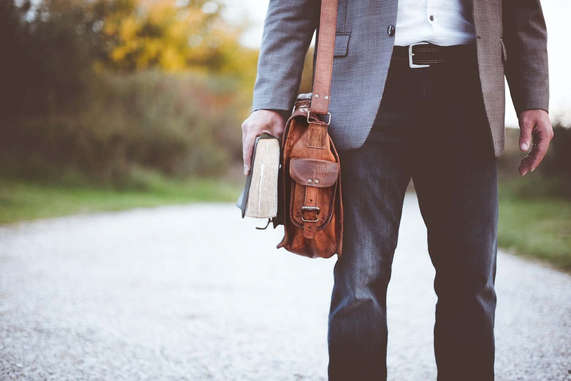 A man in a business outfit carries a briefcase and a book.