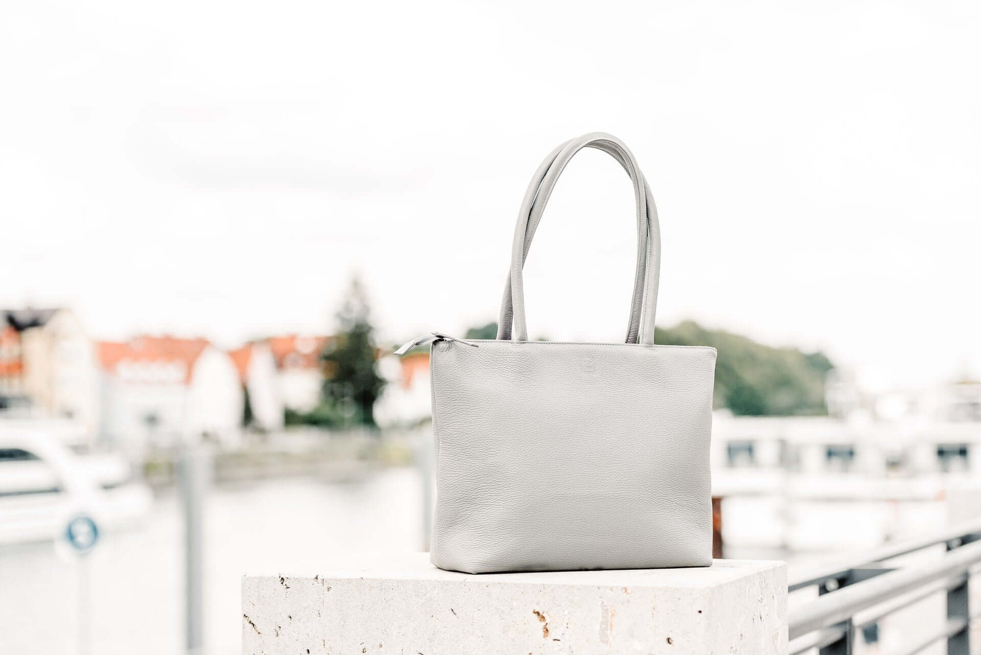 A grey tote bag propped on a wall with a suburb in the background.