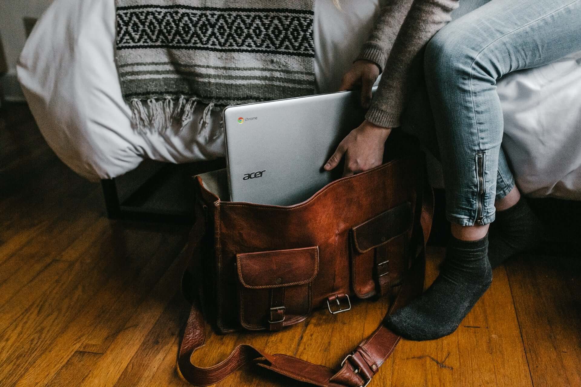 A cutoff picture of a woman in jeans putting a laptop into a leather briefcase.