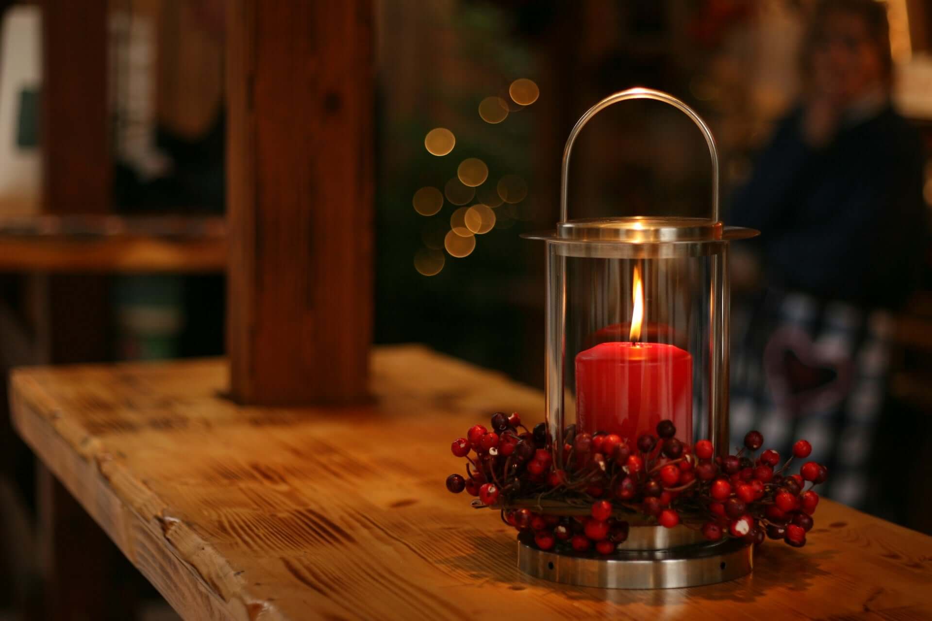 A red candle wreathed in berries sits lit on a countertop.
