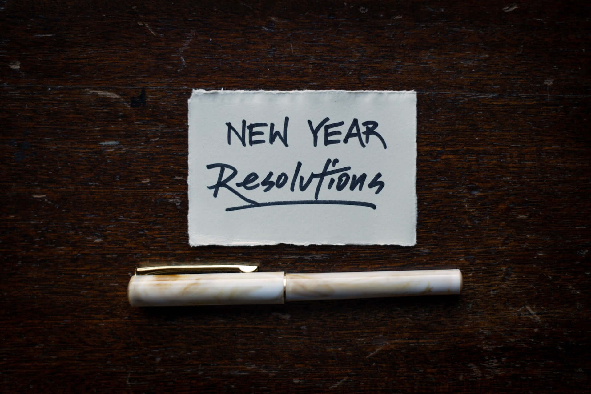 A piece of paper with "New Year Resolutions" written on it. A capped pen lies beneath it.