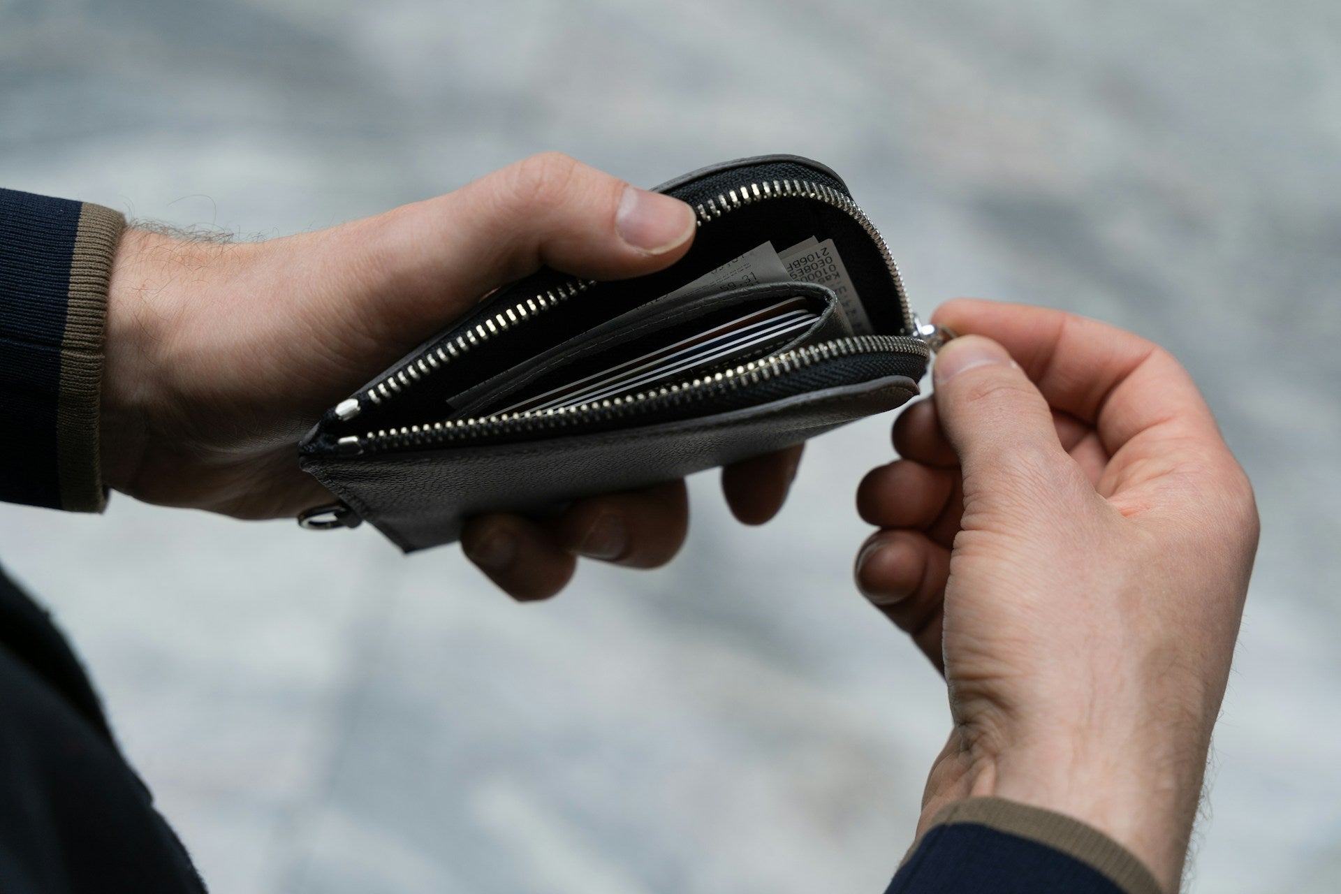 A pair of men's hands unzipping a black leather wallet to reveal folded money.