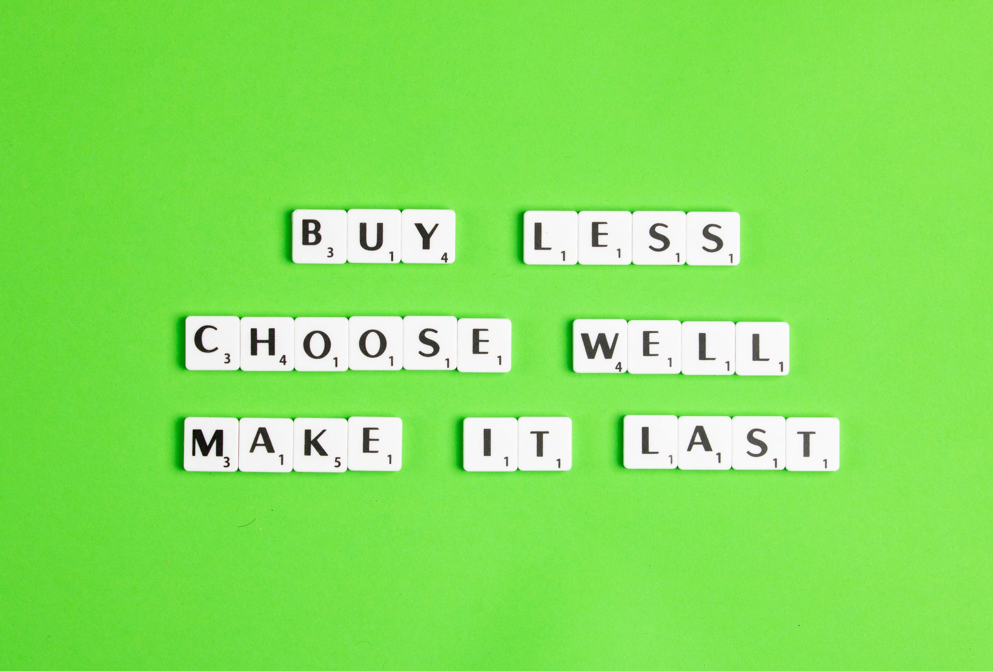 Letter tiles on a green background that spell out "Buy less, choose well, make it last."