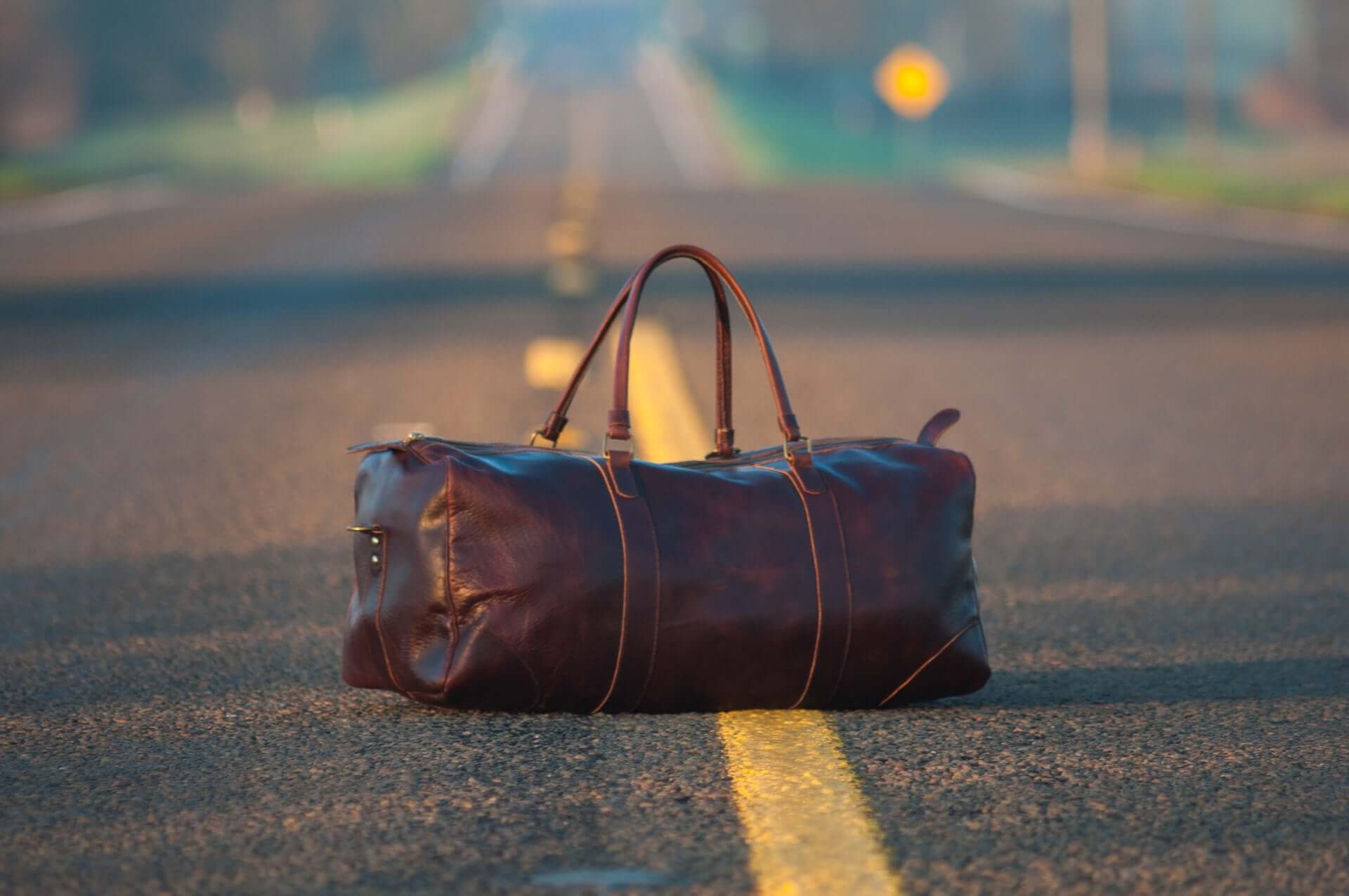 A brown leather duffel bag in the middle of a road.