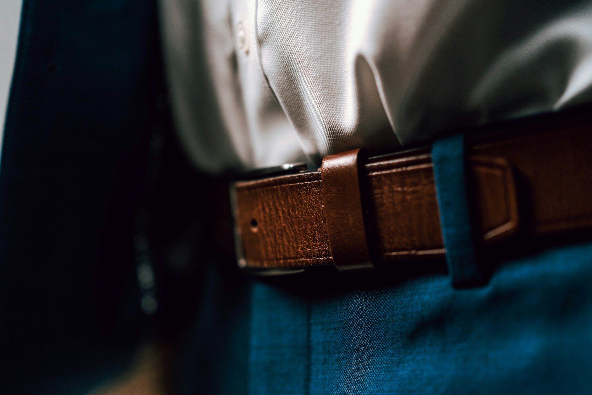 Close shot of a man in blue trousers and a brown belt.