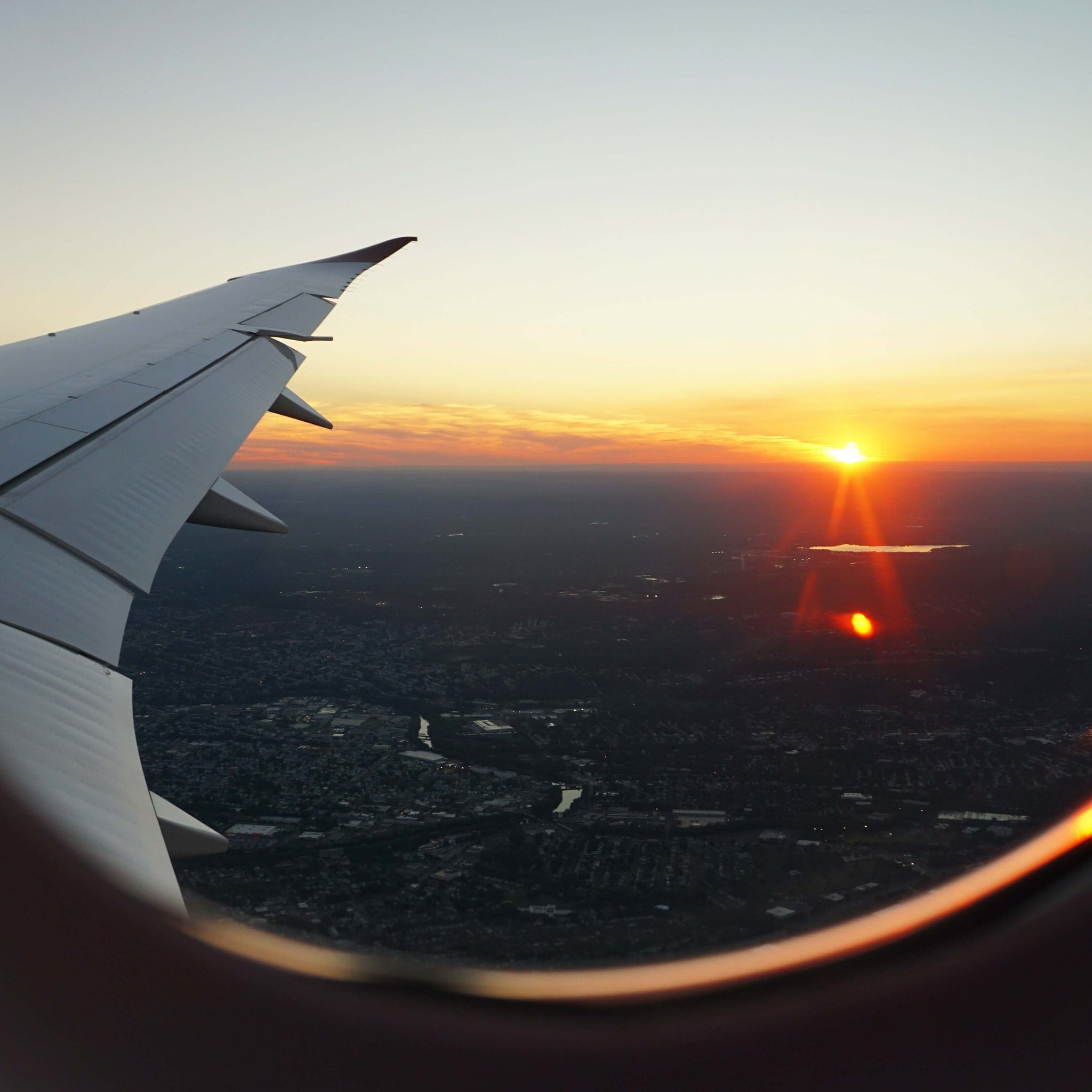 View out of a plane window over the wing. It is sunset over a forest. Via Unsplash.