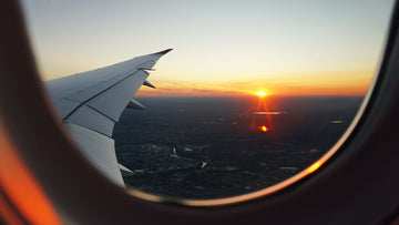 View out of a plane window over the wing. It is sunset over a forest. Via Unsplash.