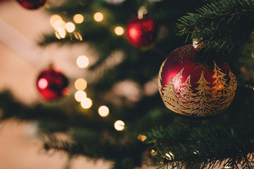 Closeup of a red and gold bauble hanging from a Christmas tree.