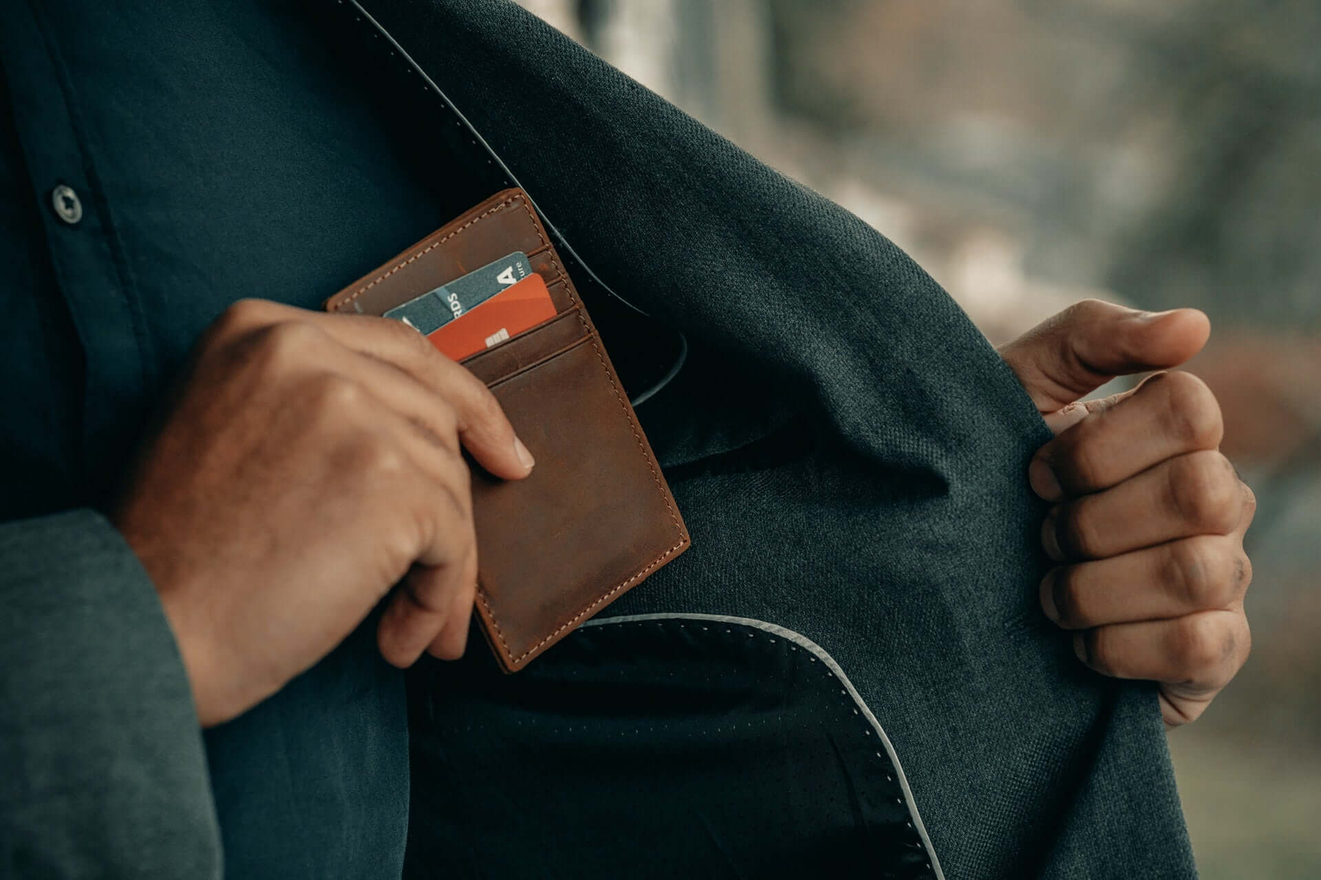 A man in a black coat inserts a brown cardholder wallet into an inner pocket.