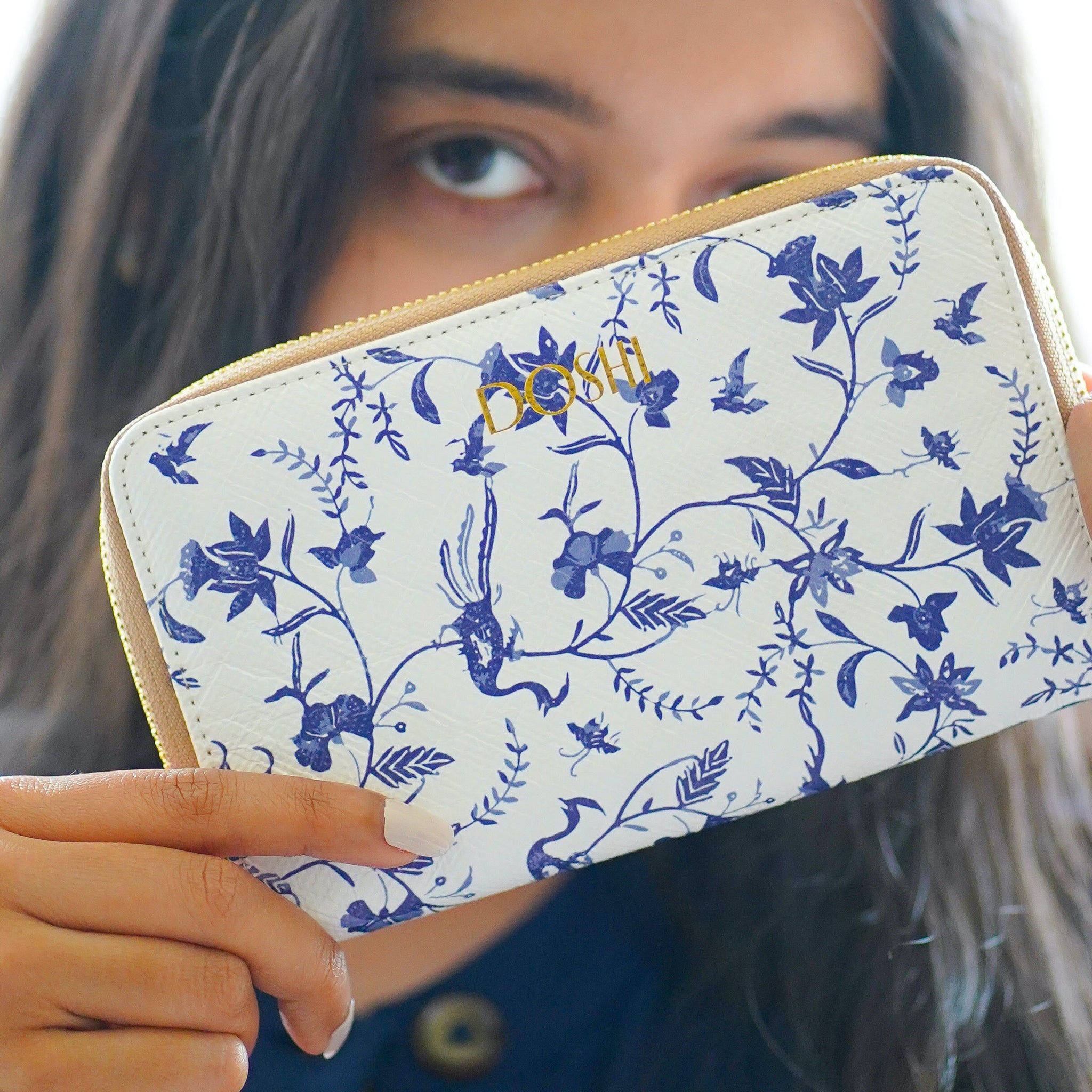 A woman modeling Doshi's Kraft Paper Continental Wallet, a full-zip wallet with a blue floral pattern on a white background.