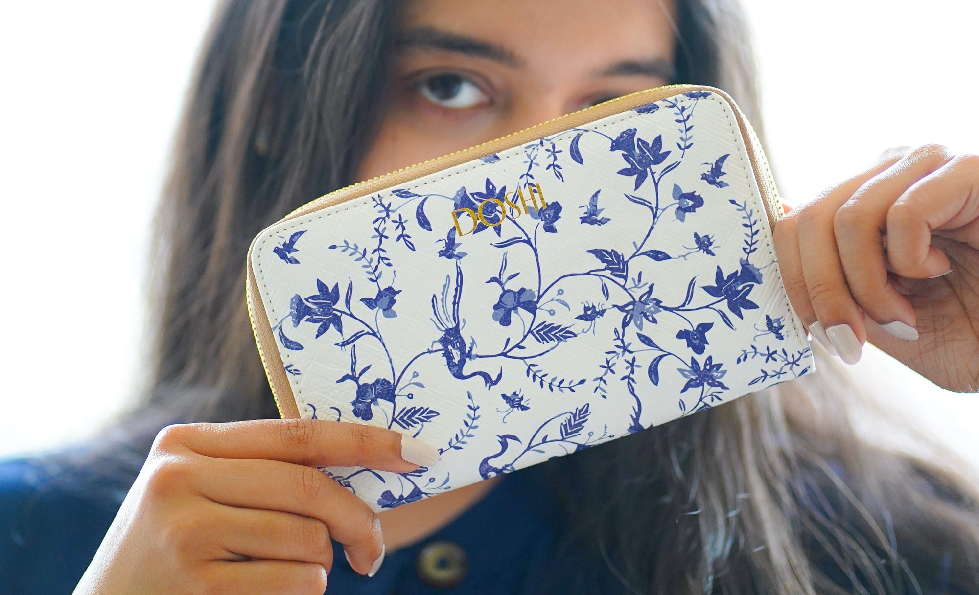 A woman modeling Doshi's Kraft Paper Continental Wallet, a full-zip wallet with a blue floral pattern on a white background.