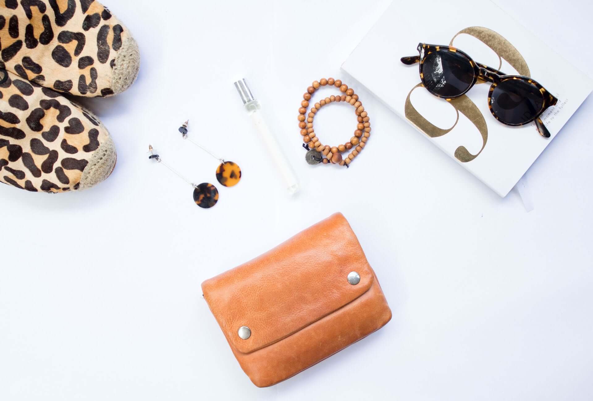 An overhead shot of various accessories including a tan wallet, sunglasses, leopard-print shoes, and jewelry.