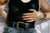 A woman's torso. She wears a black tank top, jeans, a thick black belt with statement buckle, and has orange long nails.