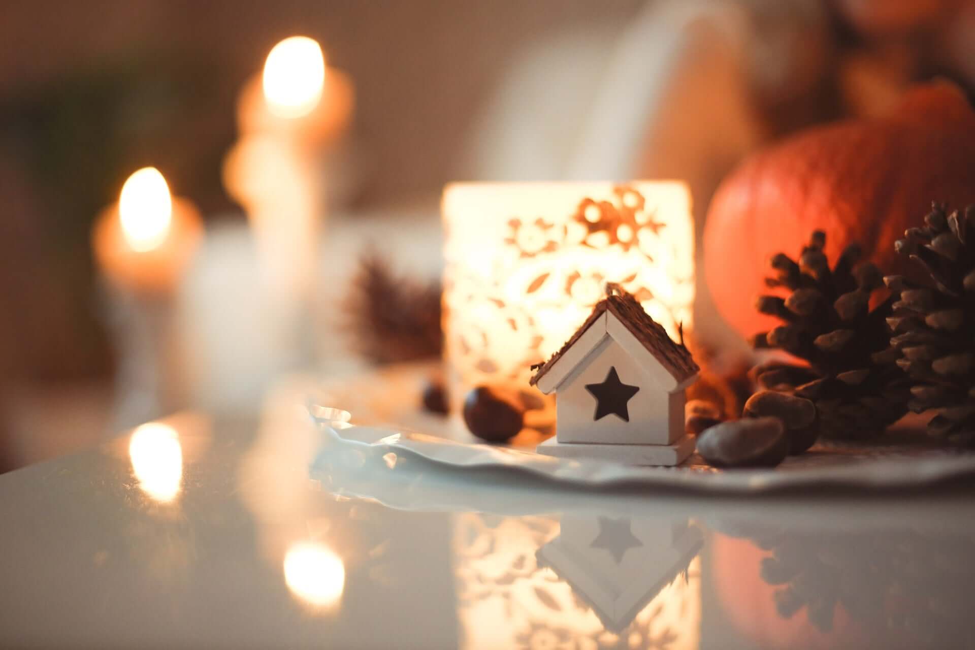 A table decorated with holiday items like pine cones, candles, baubles, and a small house ornament.