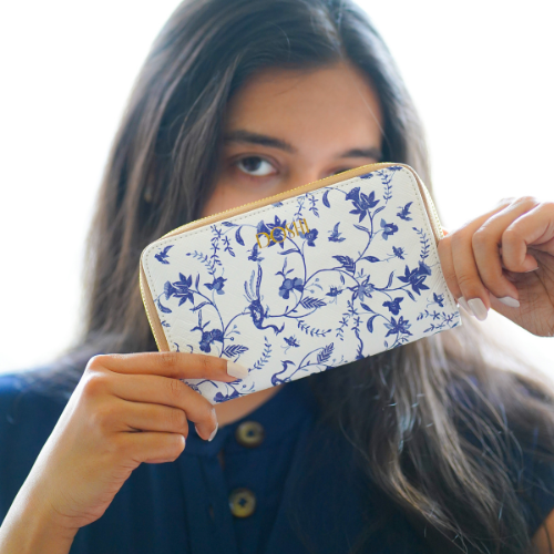 A woman holds a white continental wallet with blue floral print in front of her face.