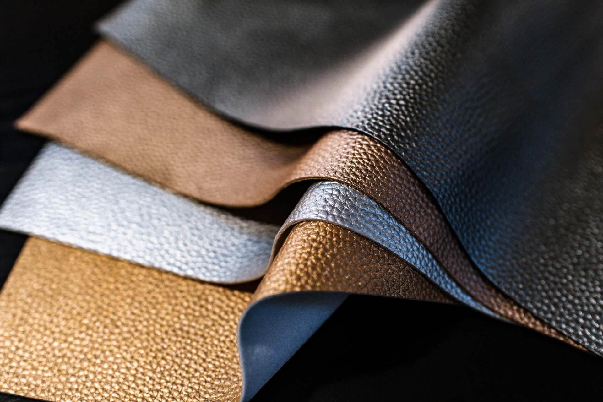 Four sheets of leather, in black, tan, silver, and gold.