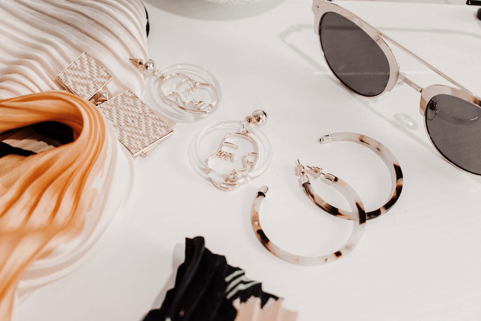 A flatlay of various accessories including hoop earrings and a pair of sunglasses.