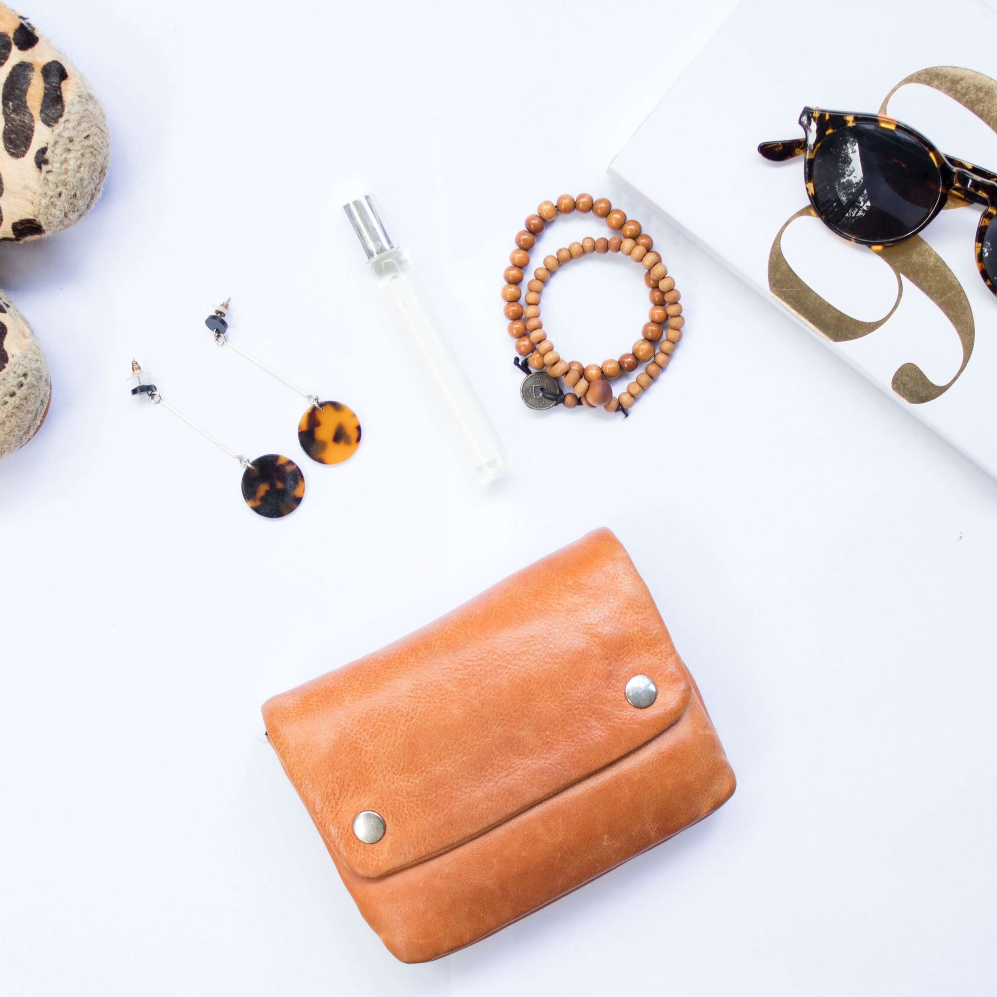 A flat layout of various women's accessories including a small handbag, sunglasses, shoes, and a set of earth-toned jewelry.