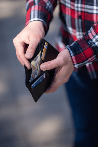 A man in a red flannel shirt holds open a black bifold wallet to reveal cash and two cards.