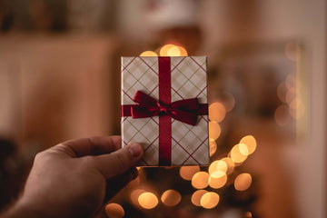 A hand holds up a small gift box wrapped in red ribbon.