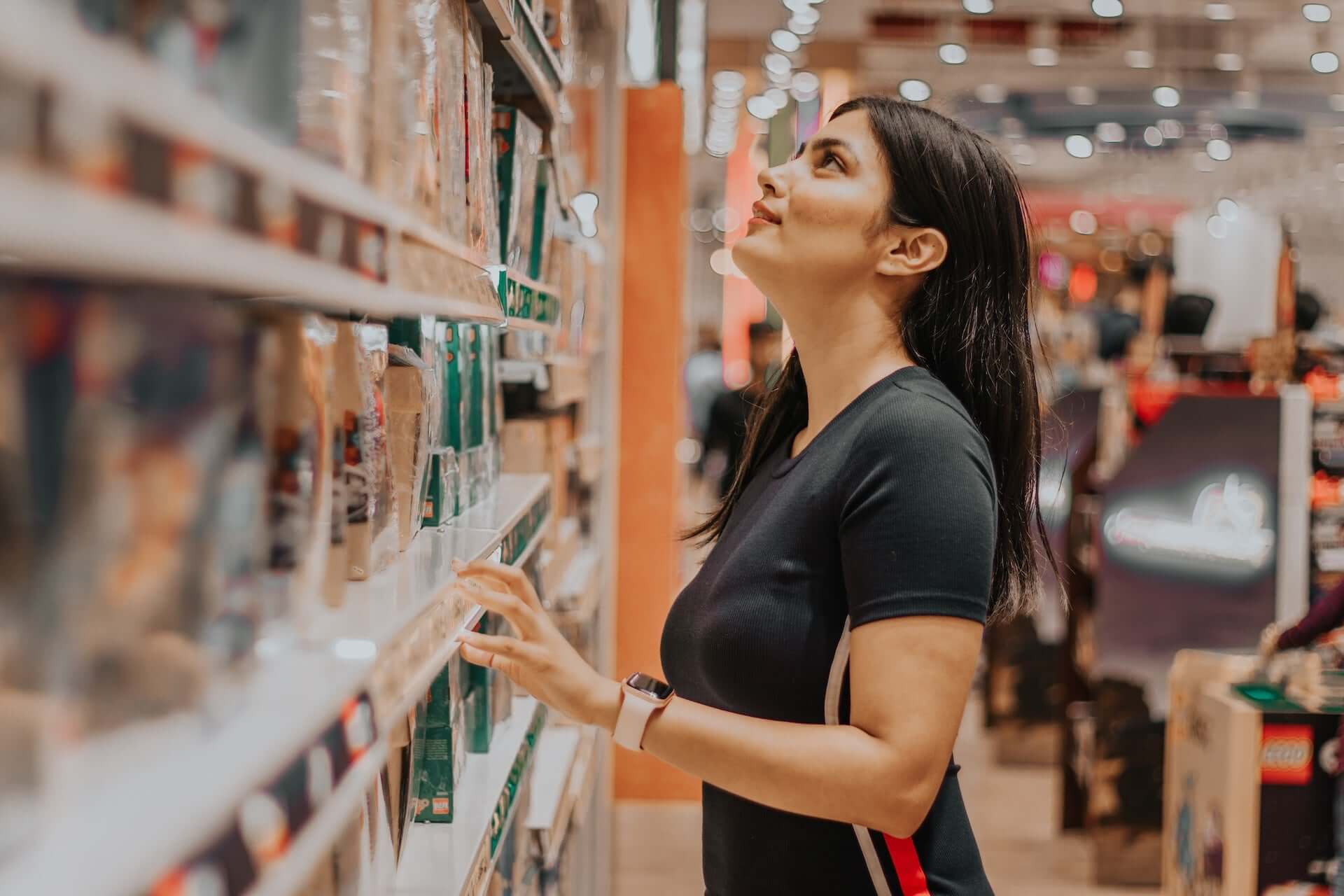 A woman stands in the personal care aisle of a grocery store, looking at body washes.