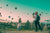 A woman in a long dress watches hot air balloons fly while a man in a hat and wearing a backpack takes pictures of her.