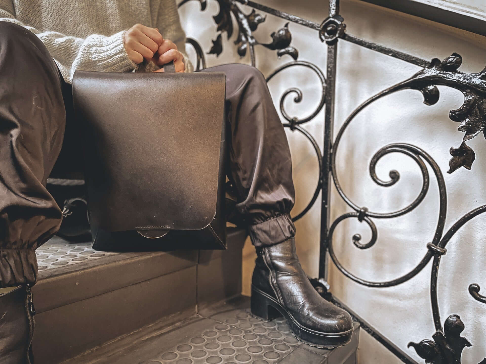 A woman in combat boots holds a grey-brown briefcase in front of her.