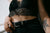 A woman's torso. She wears a black lace bralette and black jeans with a black belt.