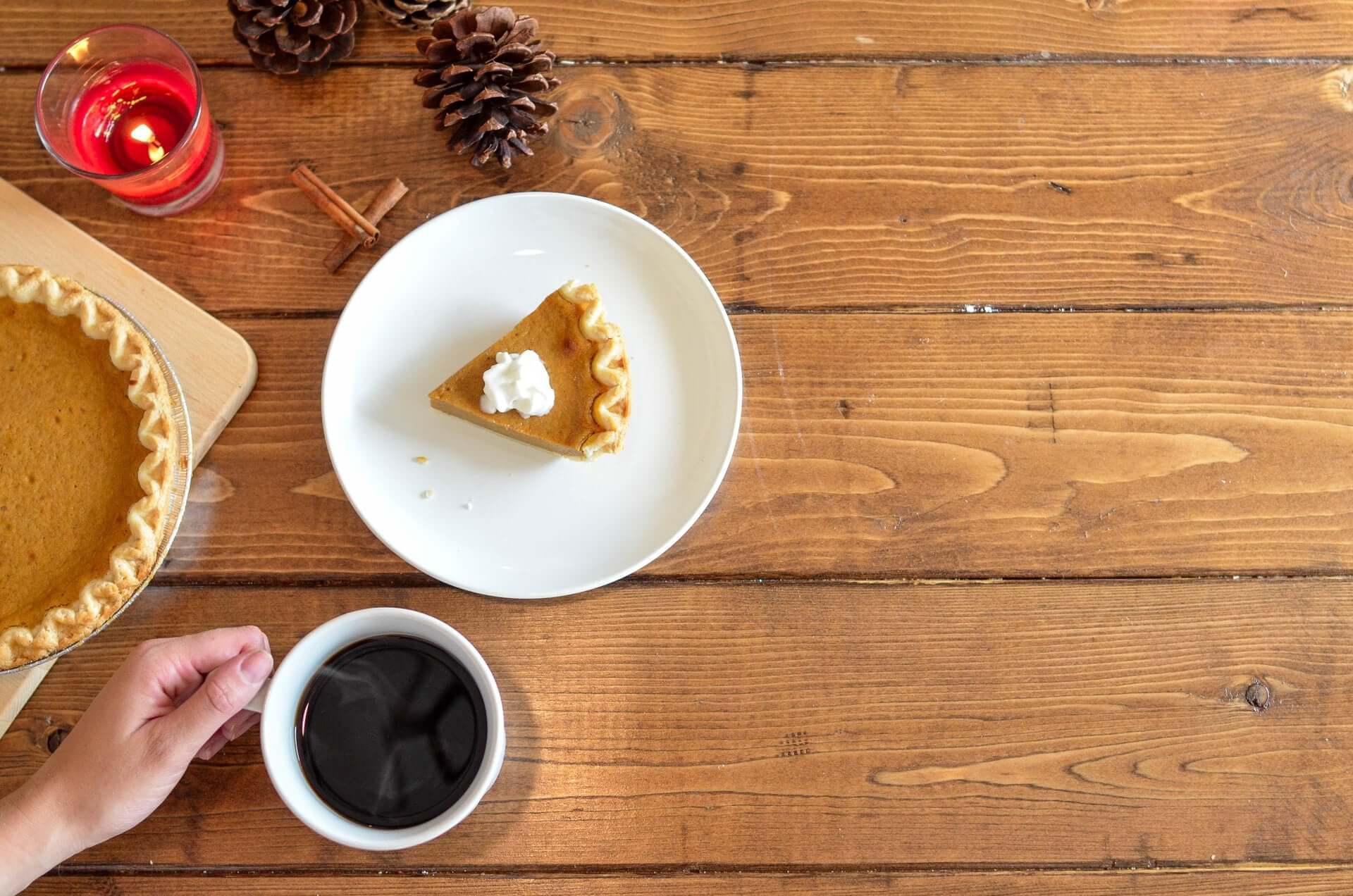 A piece of pumpkin pie on a white plate against a wood panel table.