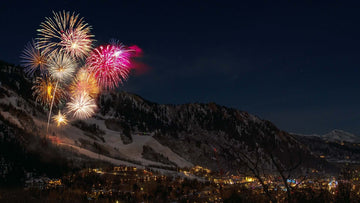 Multicolored fireworks go off on a snowy mountain side.