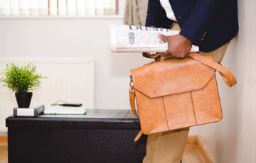 A cutoff image of a man in business attire holding a tan briefcase and a newspaper.