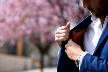 A man in a blue blazer puts a brown leather wallet in his interior coat pocket.