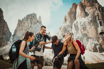 Four people laugh and play in front of a high cliffside.