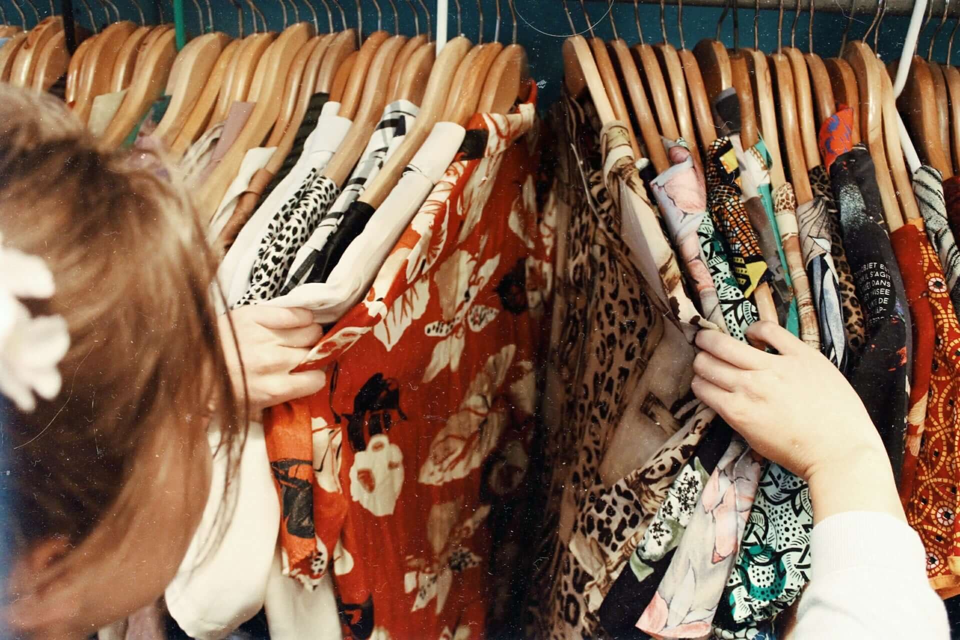 A woman looks through a rack of multicolored and patterened blouses.