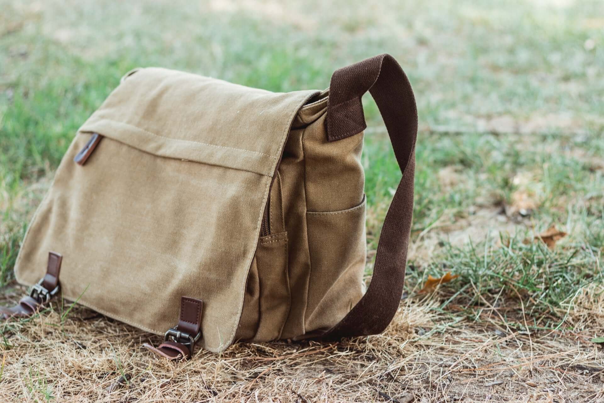 A canvas messenger bag sitting in the grass.