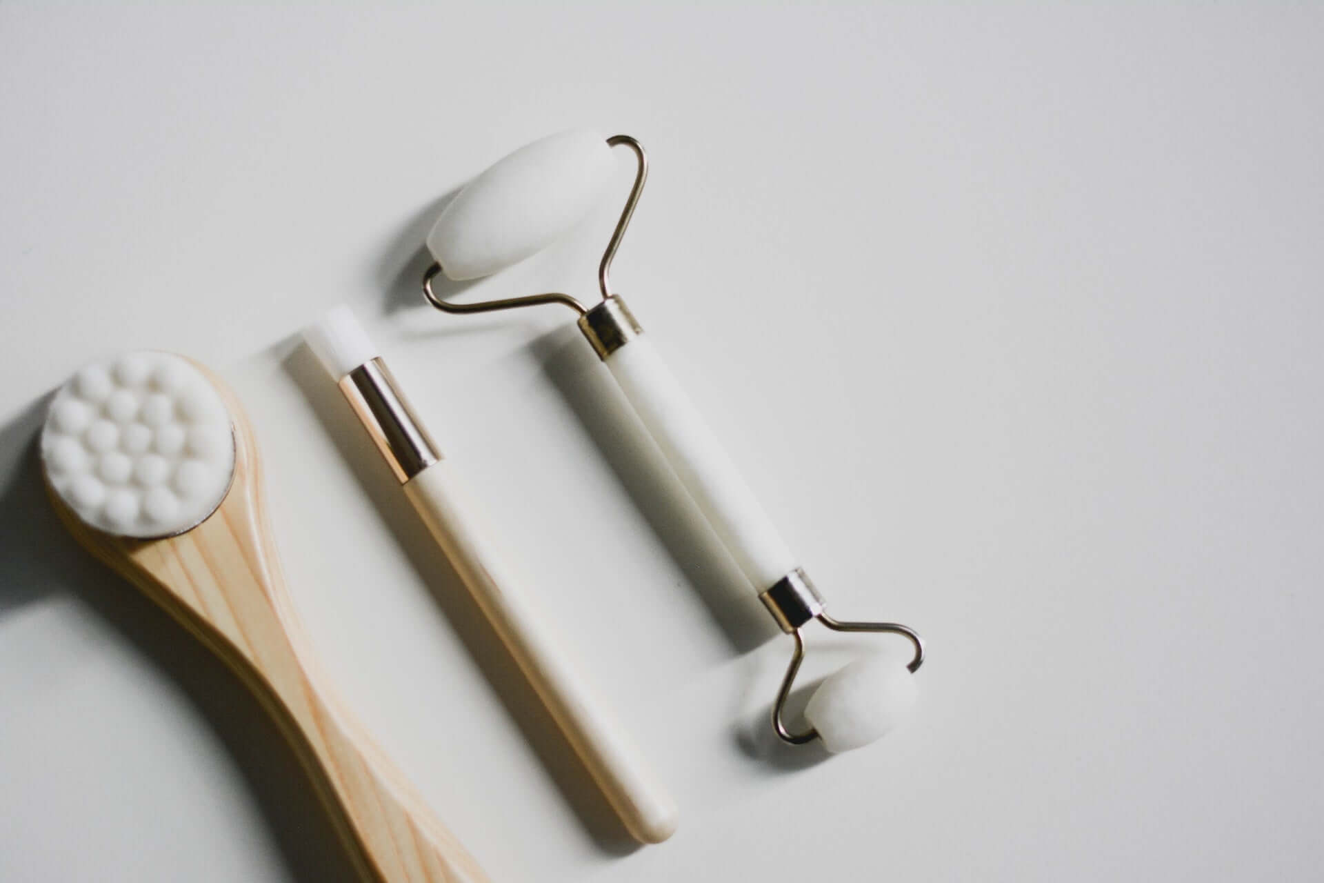 A face brush, shadow makeup brush, and face roller on a grey background.