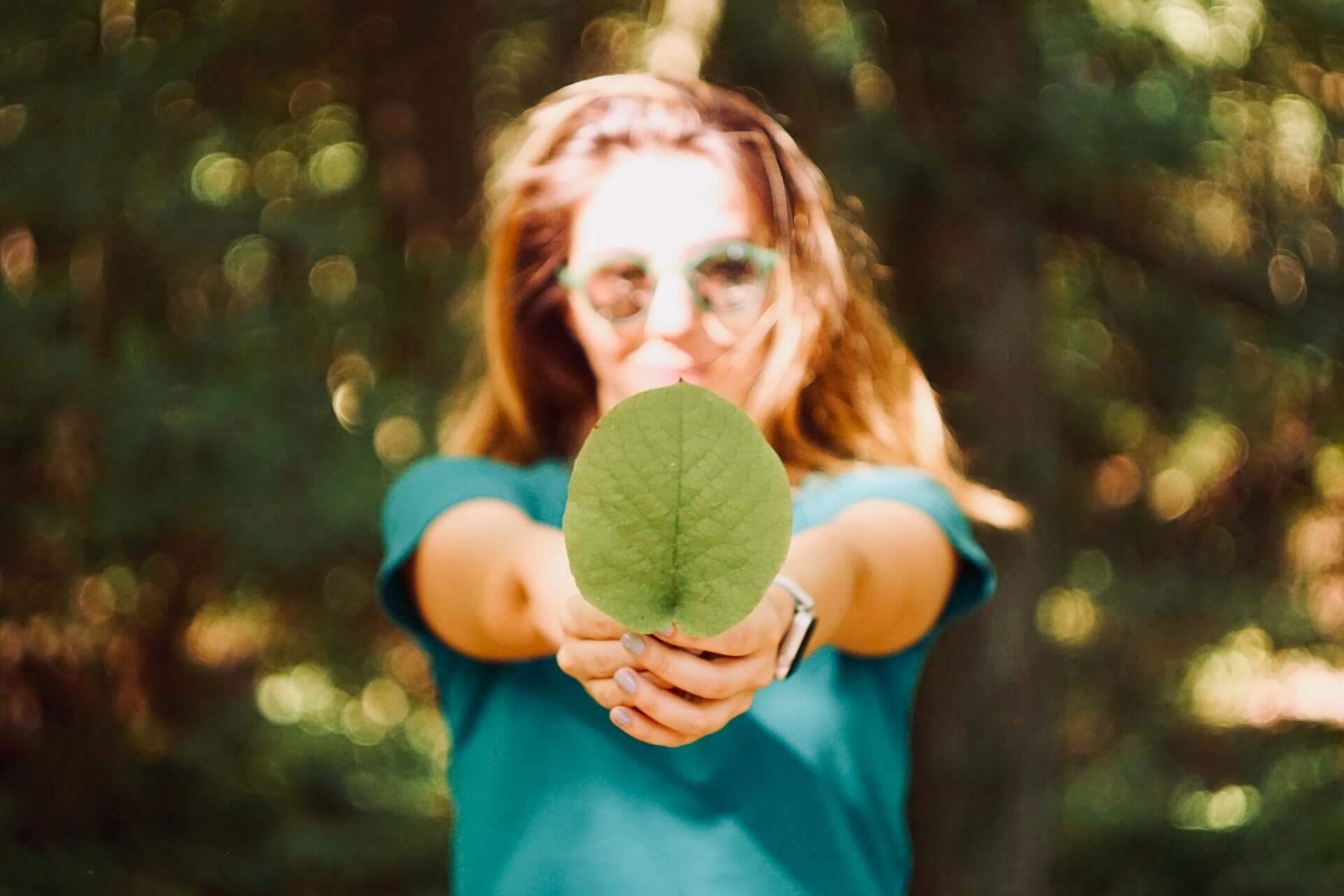 A woman in a blue t-shirt and sunglasses holds a leaf out to the camera.