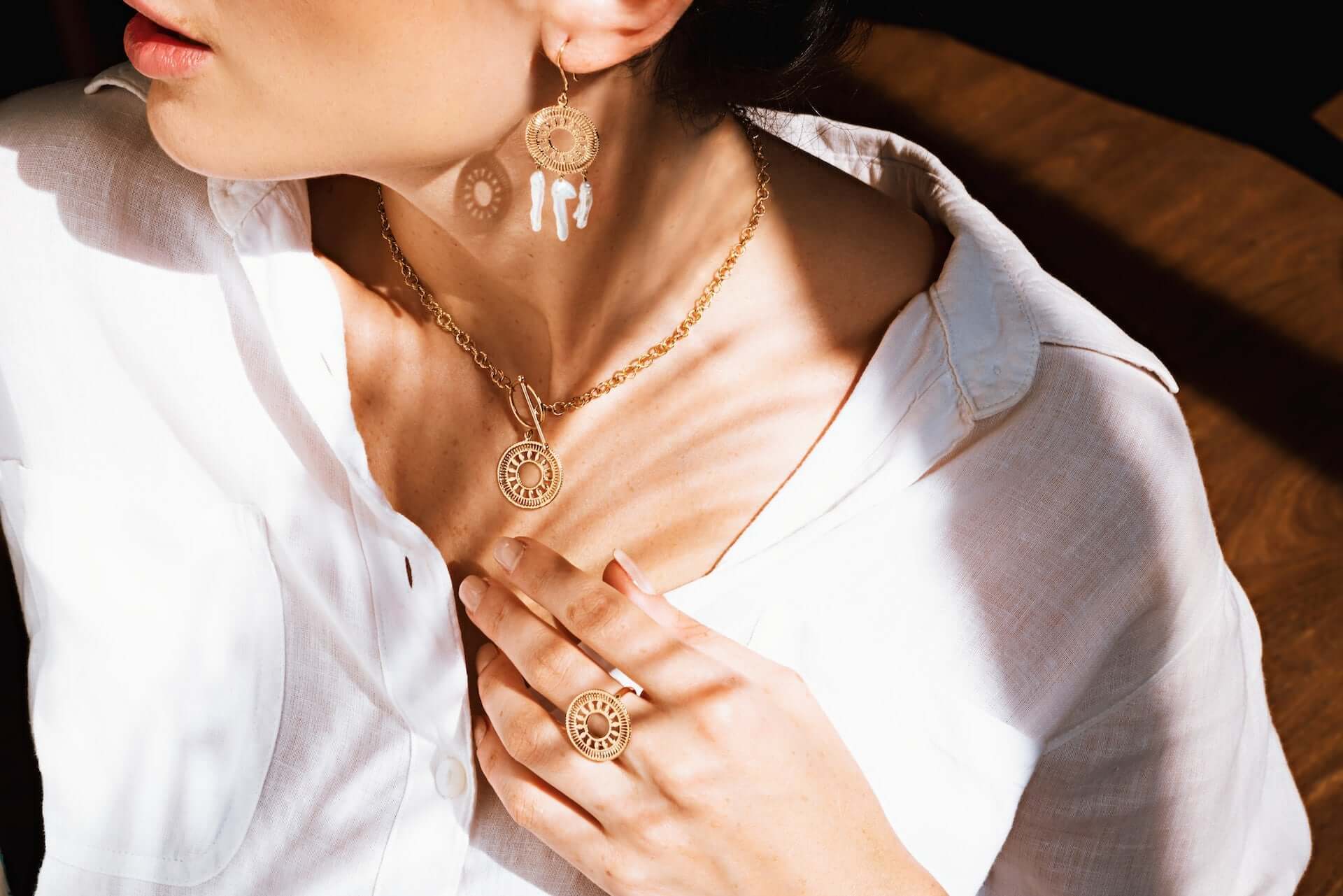 A woman in a white button down top wearing gold jewelry with white and clear stone accents.