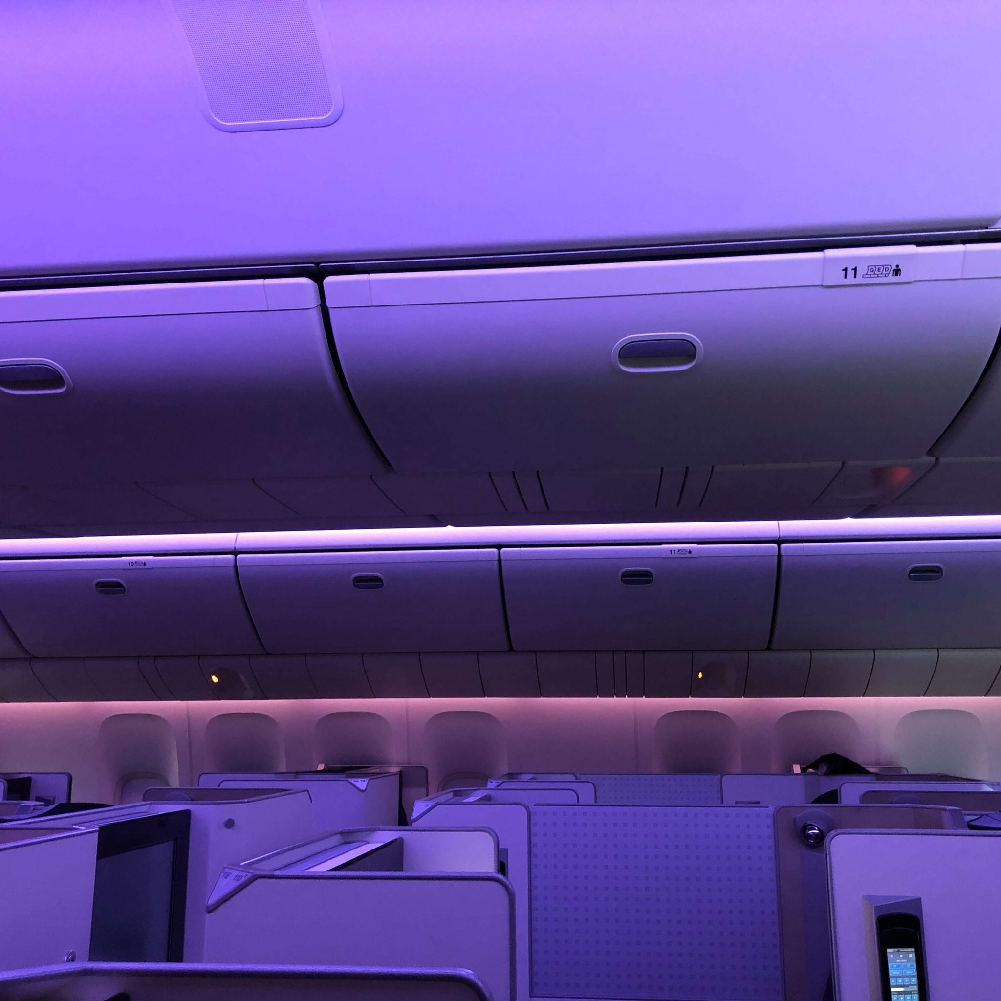 A purple-tinted image of seats in the first class cabin of an airplane.