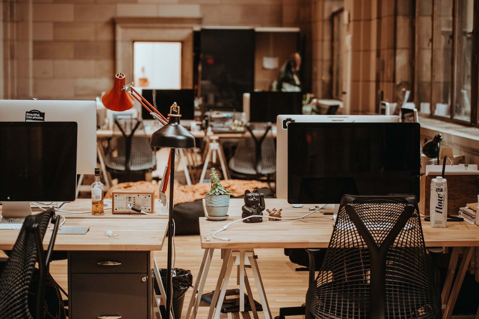 An office space with desktop computers on wooden desks. The aesthetic is relatively warm modern.