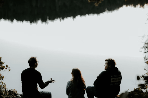 Three people silhouetted talking in front of a lake.