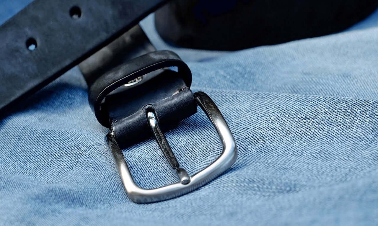 A black belt with a silver rounded buckle, sitting on blue denim.