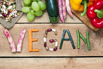 The word "Vegan" spelled out in various vegetables on a wooden surface.