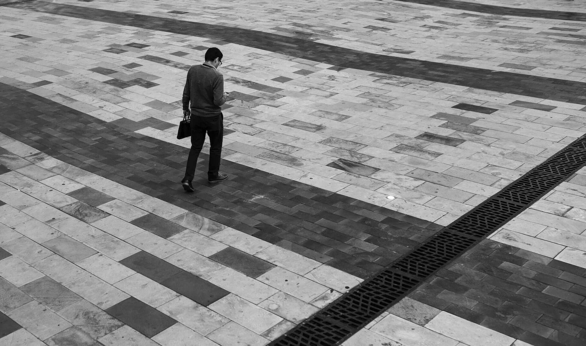 Black and white image of a man in a suit with a briefcase walking over stone paving.