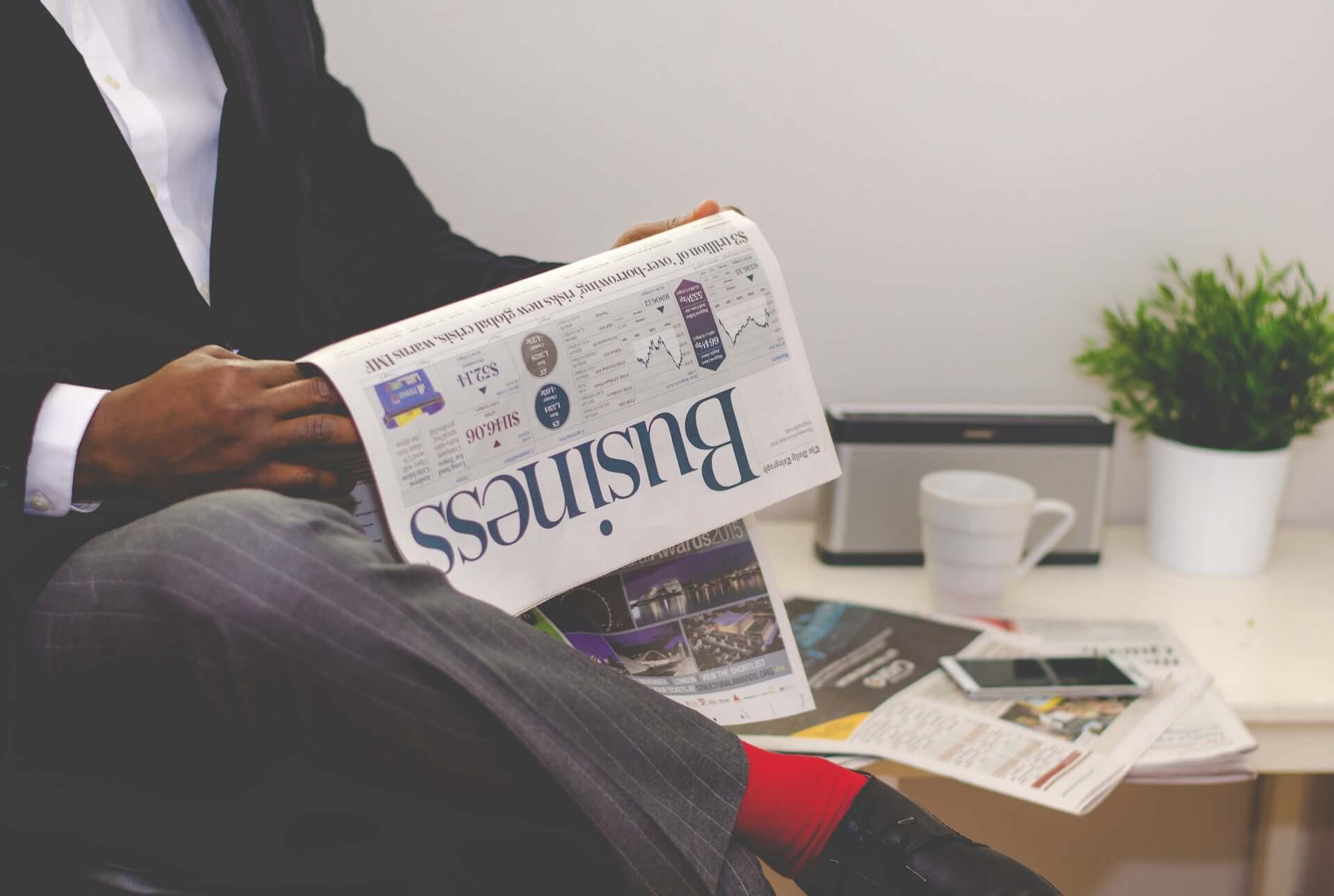 A man in a dark business suit reads the Business section of a newspaper.