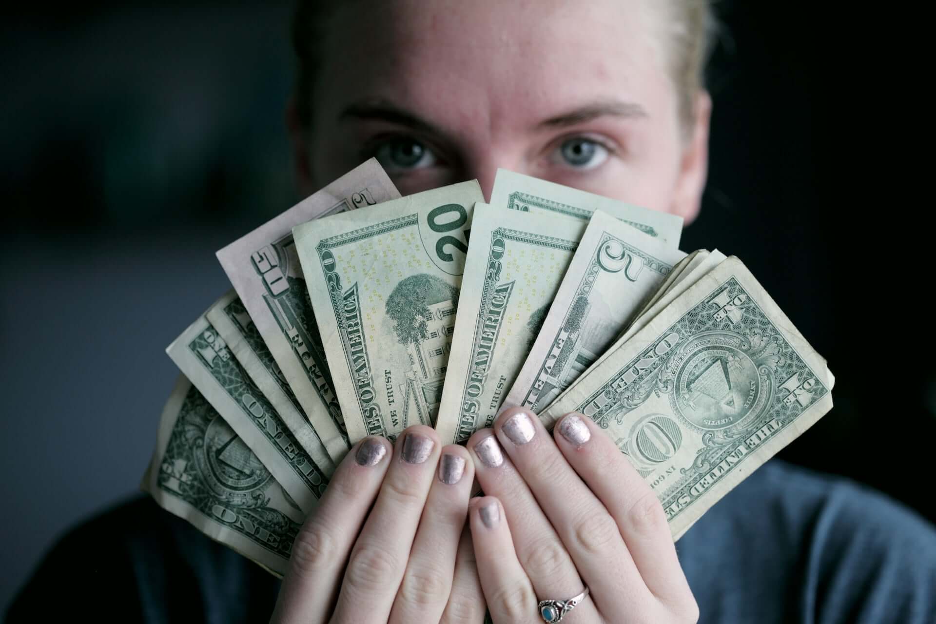 A woman fans several American dollar bills in front of her face.