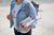 A woman in a white shirt with watermelon graphics and a denim jacket carries a backpack and schoolbooks.