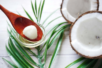 Opened coconut halves and coconut oil on a wooden spoon.