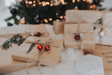 Several brown paper wrapped presents decorated with twine, red bells, and evergreeen leaves.