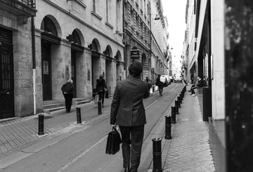 A person holding a briefcase walks down a city street. The image is in black and white.